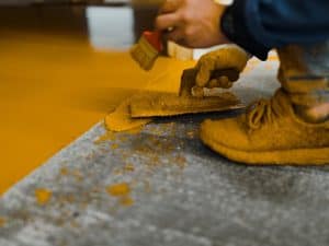 Worker applies epoxy coat on chipped epoxy floor, demonstrating repair and maintenance technique.