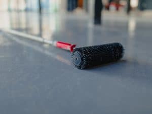 A spiked roller lying on a smooth epoxy floor, emphasising tools required for reducing epoxy floor costs.